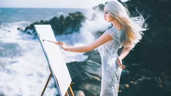 Девушка на берегу рисует на мольберте