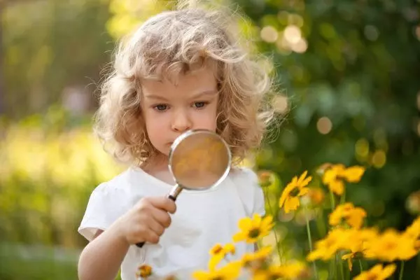 Девушка смотрит на цветок под увеличительным стеклом