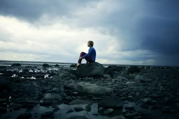 Мужчина сидит на камне у воды