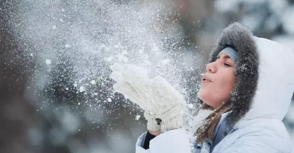 Девушка зимой сдувает ладони снегом