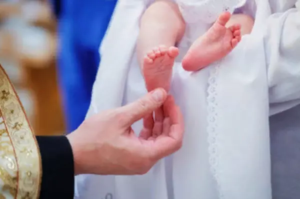 Священник касается пятки младенца