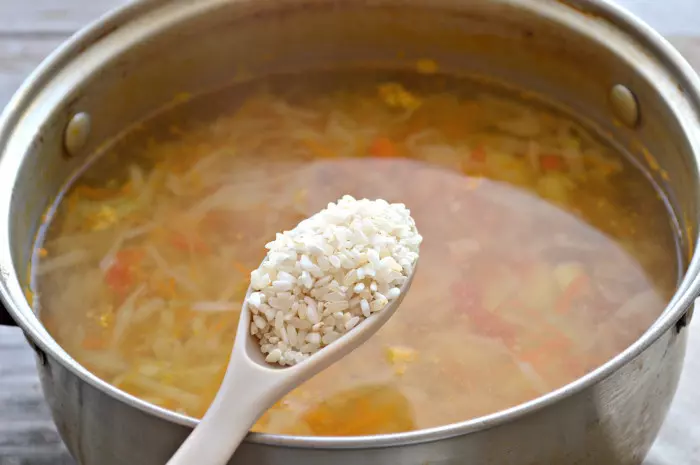Кастрюля капустного супа и ложка риса.