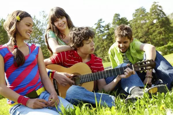 Группа подростков с гитарами сидит на траве