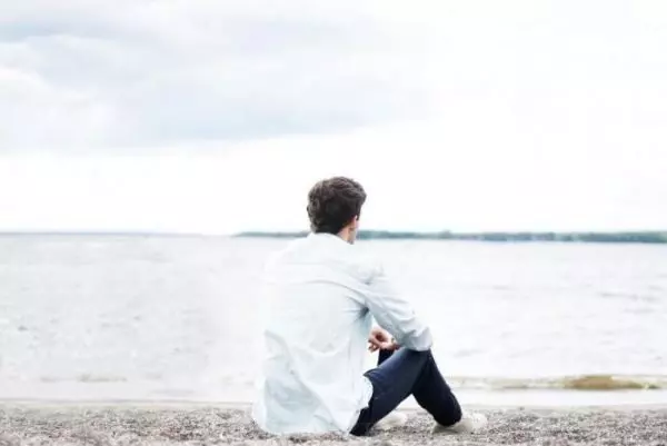 Мужчина сидит один у озера