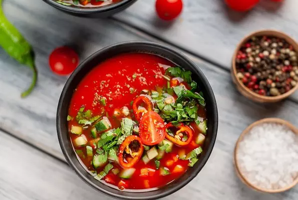 две тарелки традиционного испанского холодного томатного супа гаспачо на фоне дерева